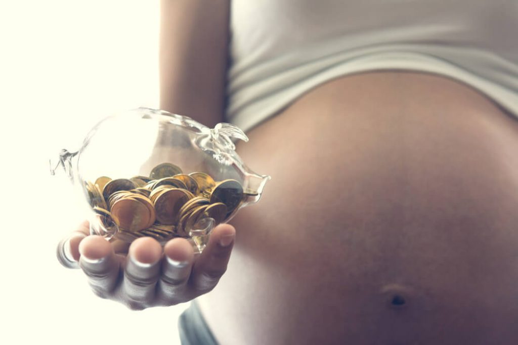 barriga de grávida segurando um pote com moedas na mão